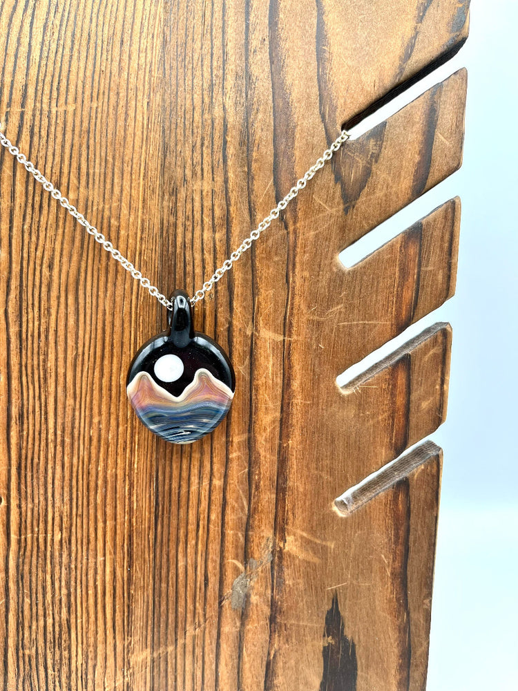 black glass double sided pendant with a landscape image of blue water, tan mountains and a white full moon in a starry sky