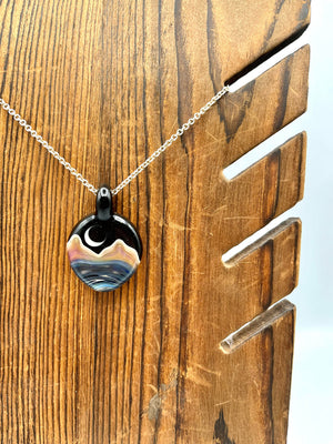 glass double sided pendant with a landscape image of blue water, tan mountains and a white quarter moon in a starry sky